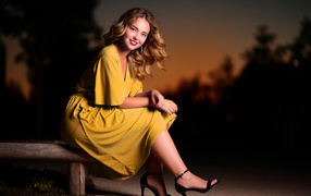 Красивая улыбающаяся девушка в желтом платье сидит на лавке 