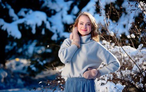 Красивая улыбающаяся девушка в варежках на фоне заснеженных деревьев 