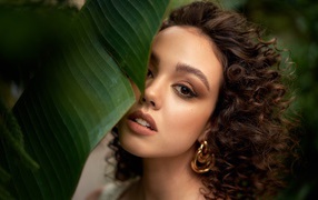 Кареглазая кудрявая девушка стоит у большого зеленого листа 