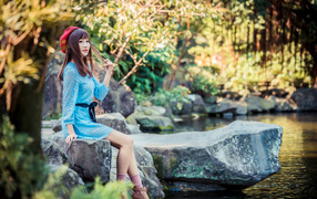 Милая азиатка в берете и синем платье сидит у воды 