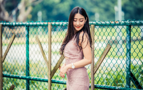 Милая азиатка в платье стоит под забором