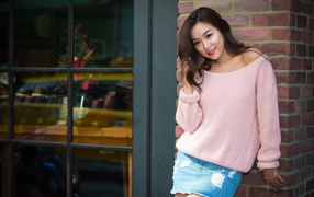 Милая азиатка в розовом свитере стоит у стены 