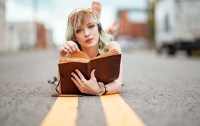 Милая блондинка лежит на асфальте с книгой 