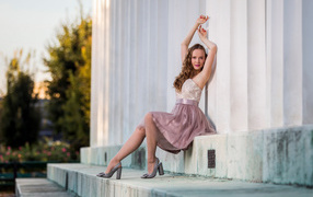 Милая девушка в юбке сидит на ступеньках у здания 