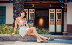 Милая улыбающаяся девушка сидит на бордюре