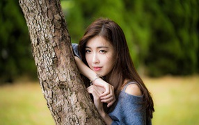 Мечтательная девушка азиатка стоит у дерева