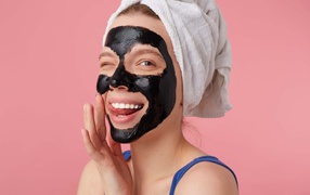 Смешная молодая девушка с черной косметической маской на лице 