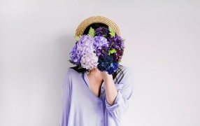 Девушка закрыла лицо букетом цветов на сером фоне