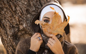 Девушка в пальто с закрывает лицо листом