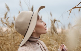 Девушка в шляпе с закрытыми глазами держит колосок 
