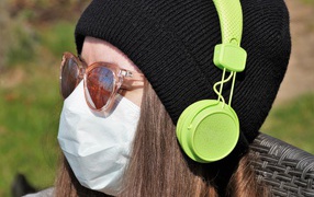 Девушка в медицинской маске на лице, в черной маске и наушниках