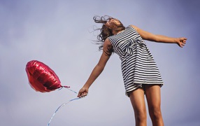 Девушка в полосатом платье прыгает с шариком 