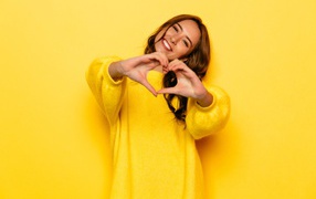 Девушка в желтом свитере показывает сердце руками