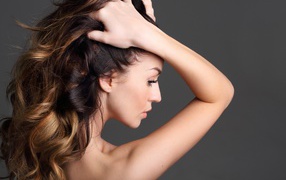 Девушка с руками в волосах на сером фоне