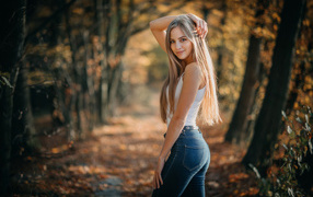 Длинноволосая блондинка в джинсах в лесу 