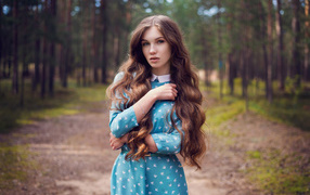 Длинноволосая девушка в голубом платье стоит в лесу