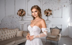 Милая девушка в свадебном платье в комнате с диваном