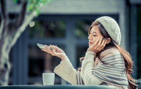 Мечтательная девушка с телефоном сидит в кафе 