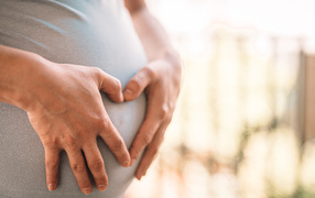 Беременная женщина держит руки на животе 