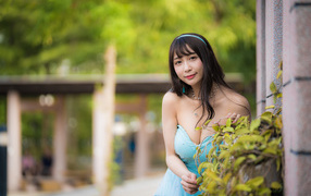 Улыбающаяся девушка азиатка в голубом платье у стены с растением 