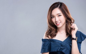 Улыбающаяся девушка азиатка с часами на руке на сером фоне