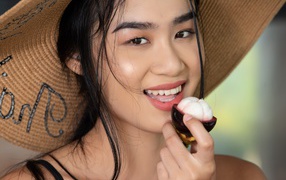 Улыбающаяся азиатка в шляпе с фруктом в руке