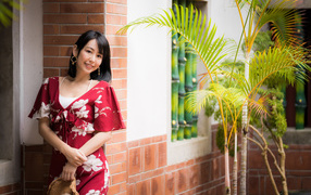 Улыбающаяся азиатка в красном платье стоит у стены 