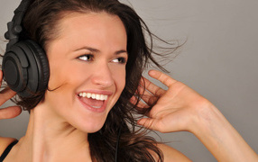 Улыбающаяся девушка в наушниках на сером фоне 