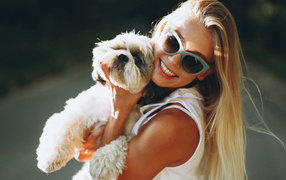 Улыбающаяся девушка в солнечных очках с собакой на руках