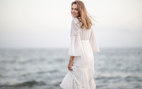 Улыбающаяся девушка в белом платье на фоне моря