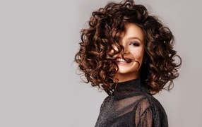 Улыбающаяся девушка с  волнистыми волосами на сером фоне