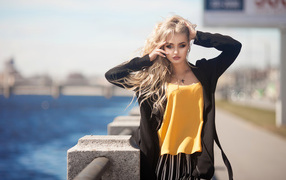 Эффектная блондинка в черном пальто стоит у воды