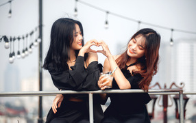 Две девушки азиатки делают сердце руками 