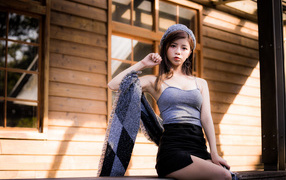 Молодая девушка азиатка в короткой юбке сидит на подоконнике 