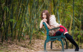 Молодая девушка азиатка сидит на зеленой лавке 