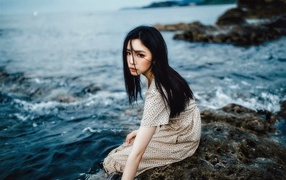 Молодая девушка азиатка сидит на камне у воды