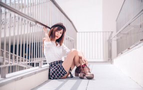 Молодая азиатка в короткой юбке сидит у перил 