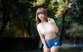 Молодая азиатка в белом топе и синих шортах  в парке