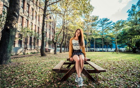 Молодая азиатка сидит на деревянном столе в парке 