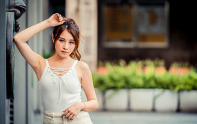 Молодая красивая азиатка в белой майке стоит у ворот