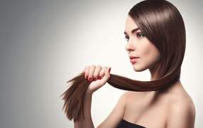 Молодая девушка держит в руках волосы на сером фоне