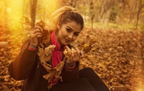 Молодая девушка с опавшими листьями в руках в парке
