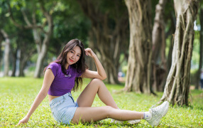 Молодая стройная азиатка сидит на земле в парке
