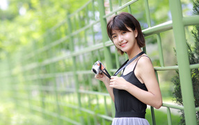Young smiling asian with a camera at the fence