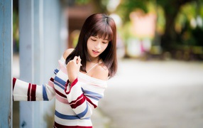 Молодая нежная девушка азиатка в свитере стоит у забора 