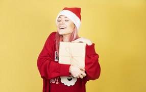 Smiling girl in a red sweater with a gift on a yellow background