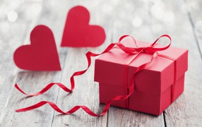 Красная коробка с подарком на столе с красными сердечками