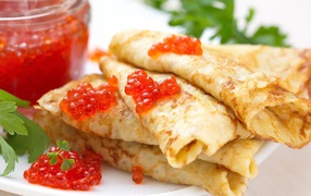Appetizing thin pancakes with red caviar on a plate with parsley. Pancake treat.