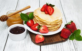 Pancakes with strawberries on a table with honey and jam for the holiday Maslenitsa 2020