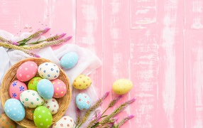 Basket with colored eggs on a pink background